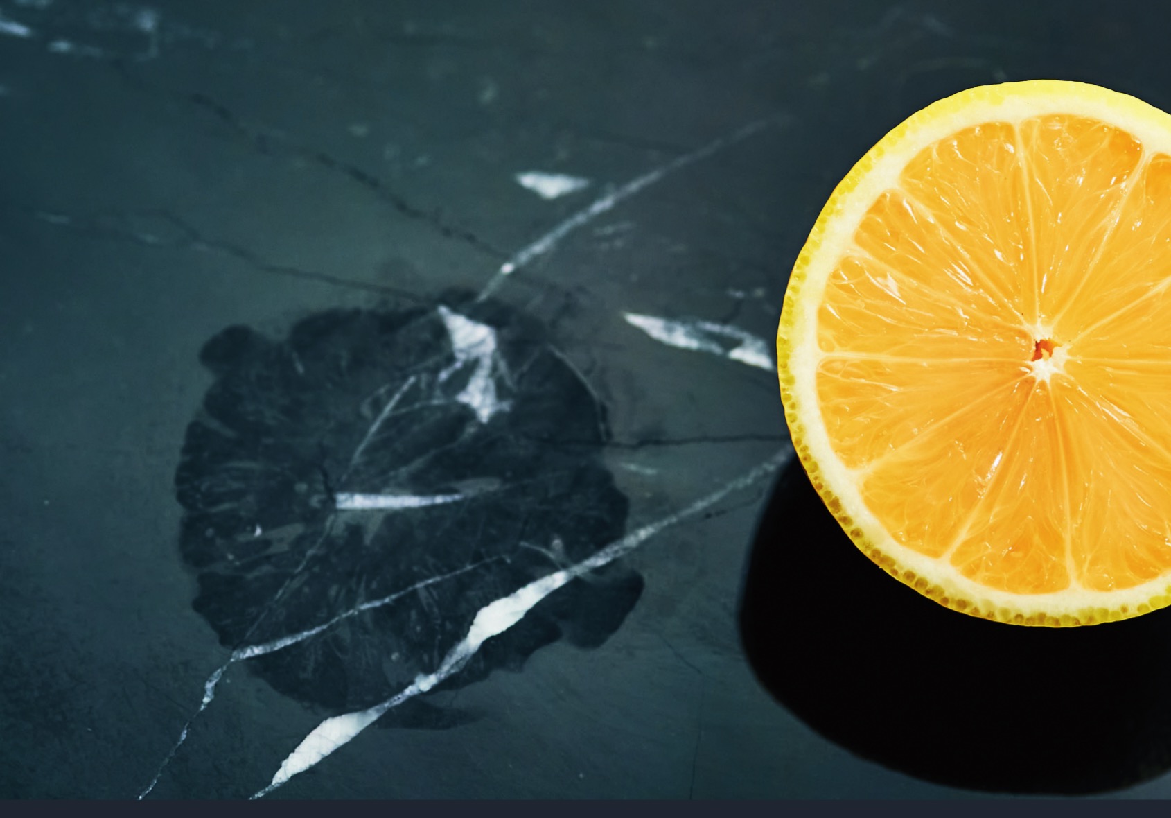 A halved lemon on dark stone next to a marble sample showing an etch ring, illustrating the acid damage AntiEtch prevents
